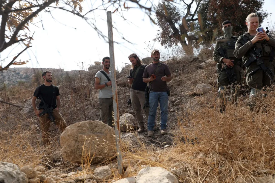 Soldados israelenses e colonos israelenses armados são vistos em um olival na cidade de Idhna, a oeste de Hebron, na Cisjordânia ocupada, Palestina, enquanto forças israelenses impedem palestinos e ativistas estrangeiros que os apoiam de colher azeitonas e os obrigam a deixar a área, em 13 de outubro de 2026. [Mamoun Wazwaz – Anadolu Agency]