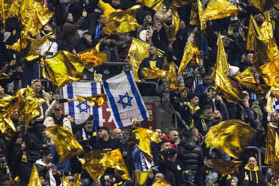 Torcedores do Maccabi exibem bandeiras amarelas ao lado de bandeiras israelenses durante a partida entre Ajax Amsterdam e Maccabi Tel Aviv, válida pela quarta rodada da fase de liga da Liga Europa da UEFA, no estádio Johan Cruijff, em Amsterdã, em 7 de novembro de 2024. [Robin van Lonkhuijsen/AFP via Getty Images]